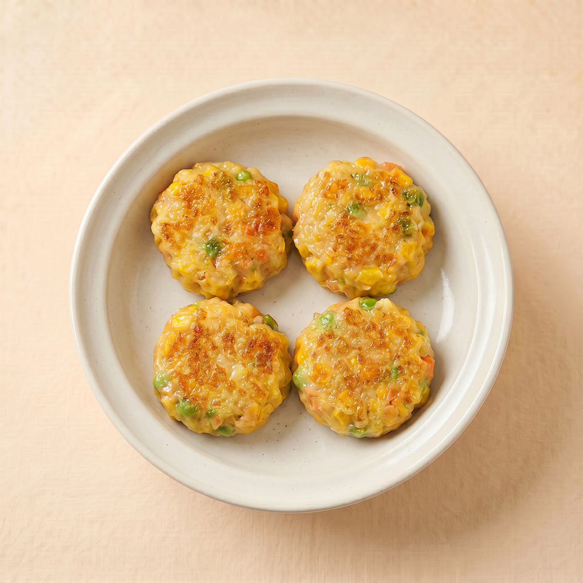 Close-up shot of pan-fried sweet corn and pork patties showing colorful green peas and bright corn kernels